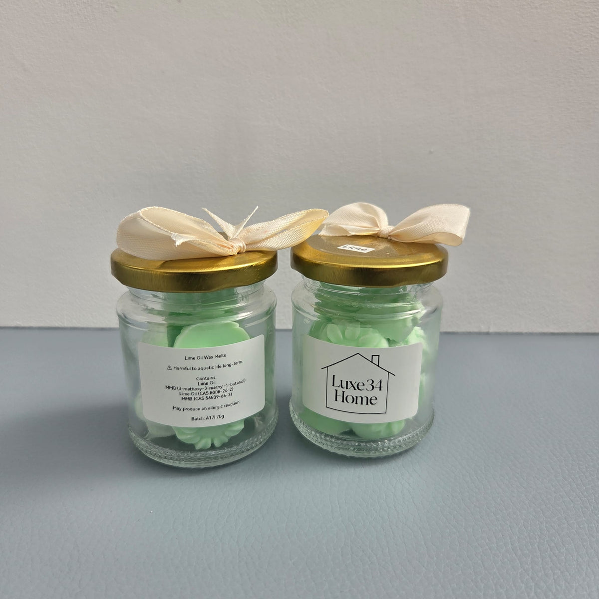 

`Two Luxe 34 Home lime wax melt jars showing front and back labels with gold lids`