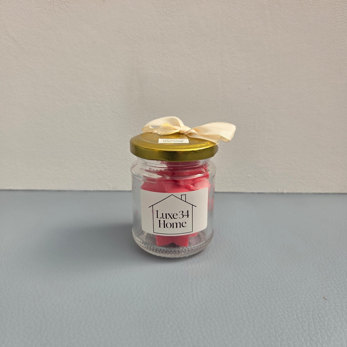 Luxe 34 Home geranium wax melts close up in glass jar with gold lid and red ribbon`