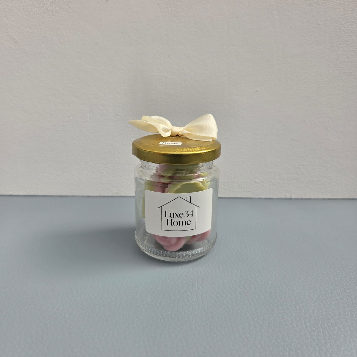 Luxe 34 Home rose wax melts in glass jar with pink and green rose-shaped wax melts, gold lid and cream ribbon