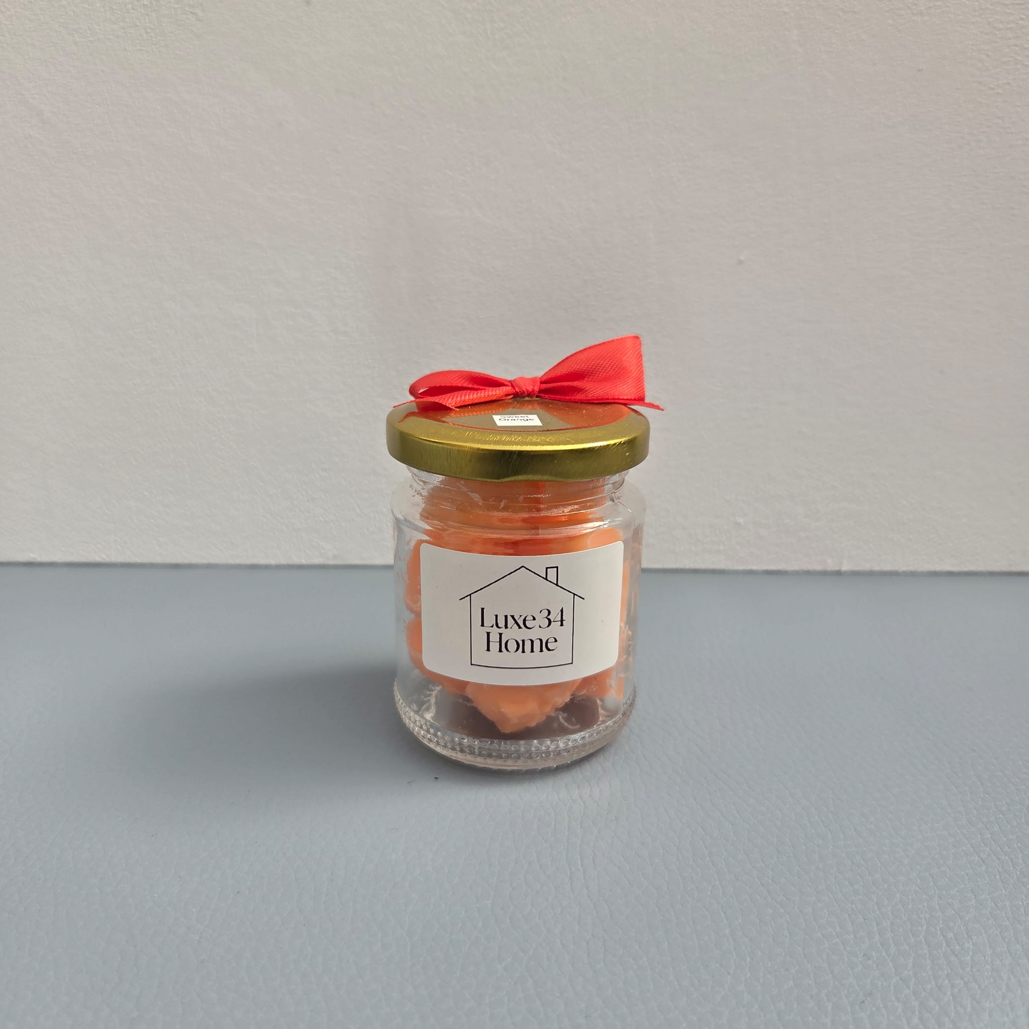 Luxe 34 Home sweet orange wax melts close up in glass jar with orange wax melts, gold lid and red ribbon
