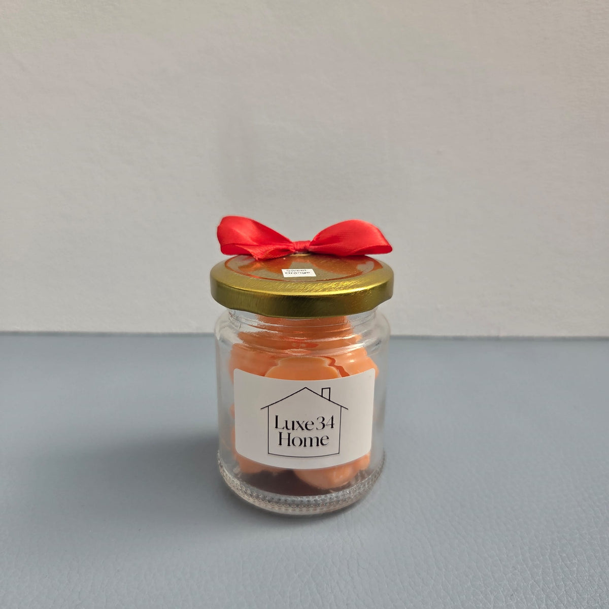 Luxe 34 Home sweet orange wax melts in glass jar with orange wax melts, gold lid and red ribbon bow