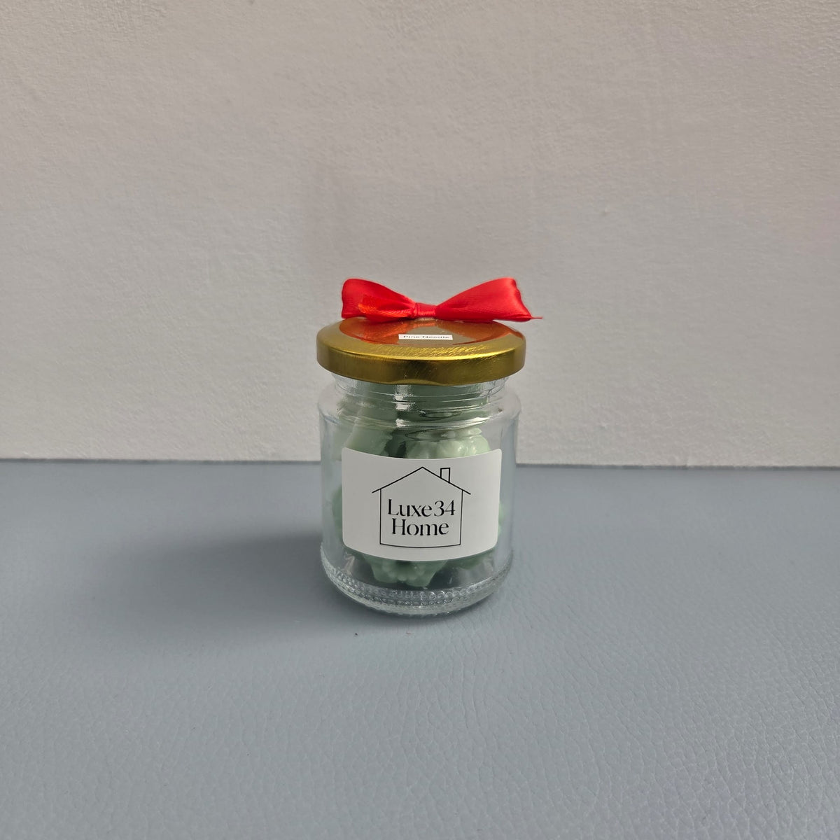Luxe 34 Home pine needle wax melts close up in glass jar with sage green wax melts, gold lid and red ribbon