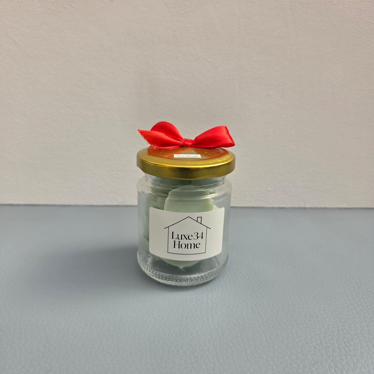 Luxe 34 Home pine needle wax melts in glass jar with sage green wax melts, gold lid and red ribbon bow