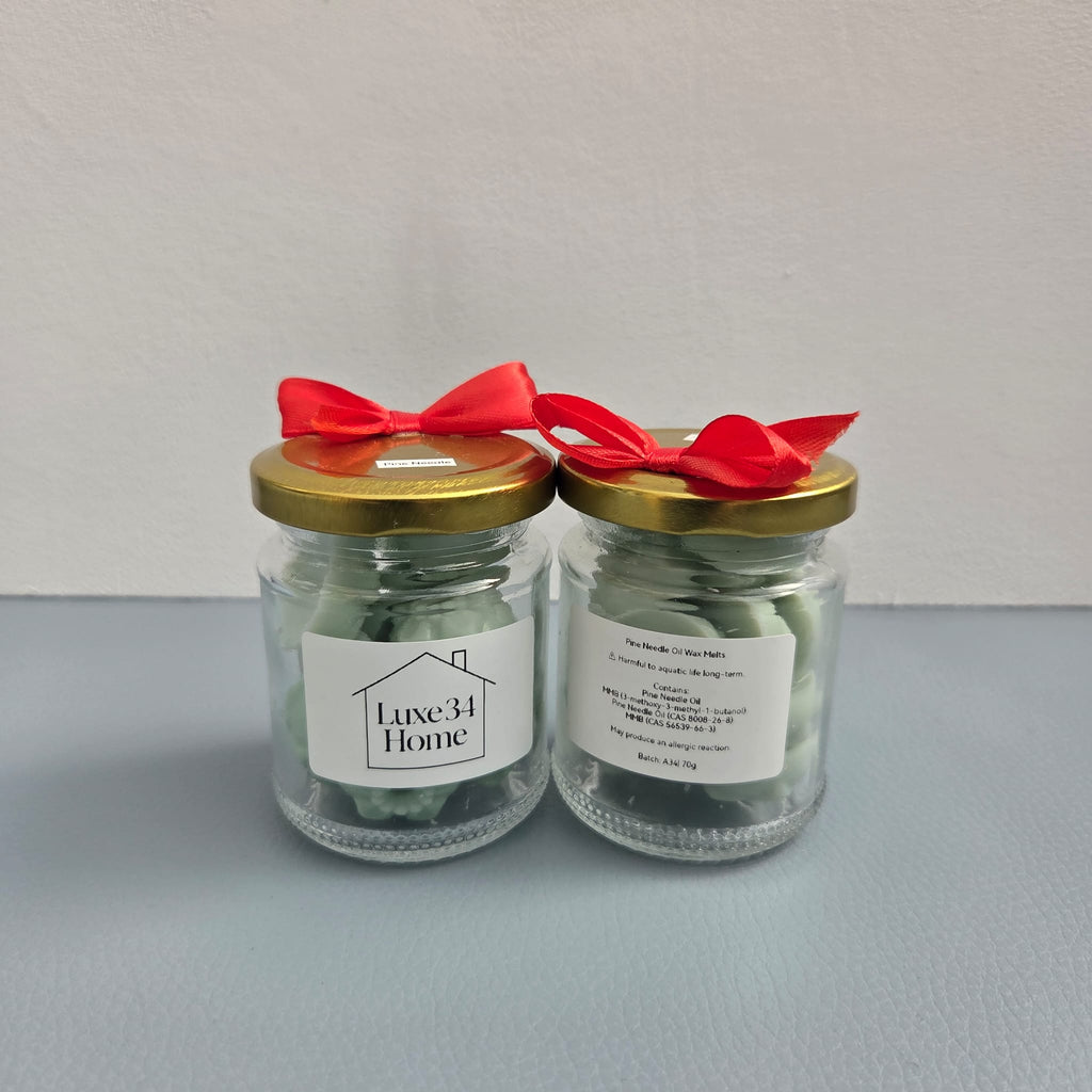 Two Luxe 34 Home pine needle wax melt jars showing front and back labels with gold lids and red ribbons