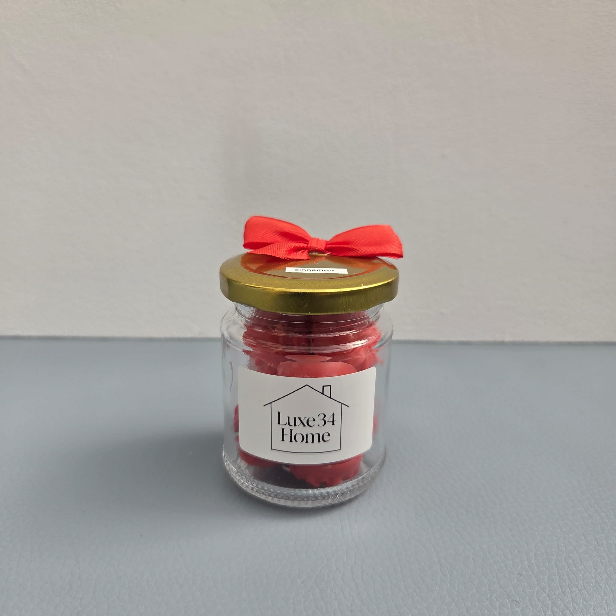 Luxe 34 Home cinnamon wax melts in glass jar with deep red wax melts, gold lid and red ribbon bow